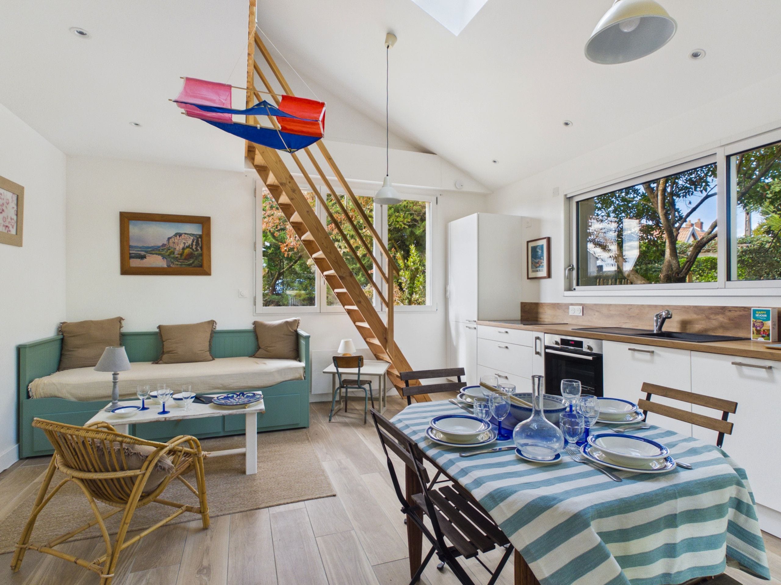 A modern kitchen with a dining area, wooden staircase, and a view of the outdoors.