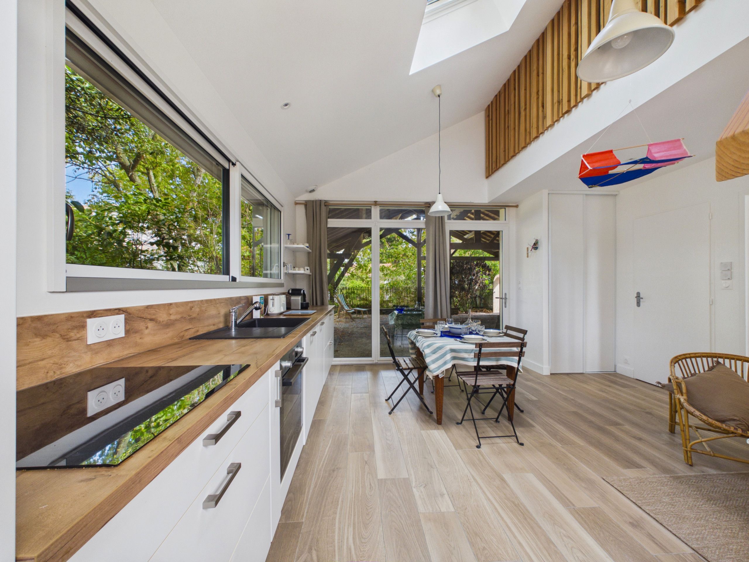 Une cuisine moderne avec une grande fenêtre, un coin repas avec une table et des chaises, et un plafond en bois.