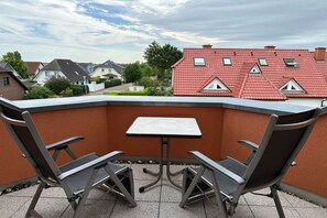 Une terrasse sur le toit, avec une table et deux chaises, entourée d’un petit muret.