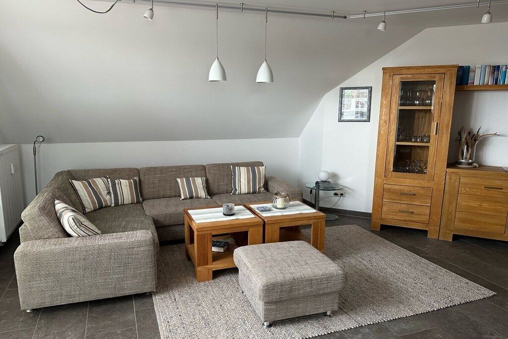 A modern living room with a sectional sofa, two wooden side tables, a matching ottoman, and a cabinet with glass doors.
