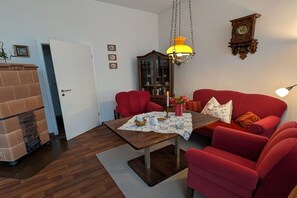 A living room with a red sofa, a wooden coffee table, and a hanging lamp. - Holiday apartment with 2 bedrooms (Norderney)