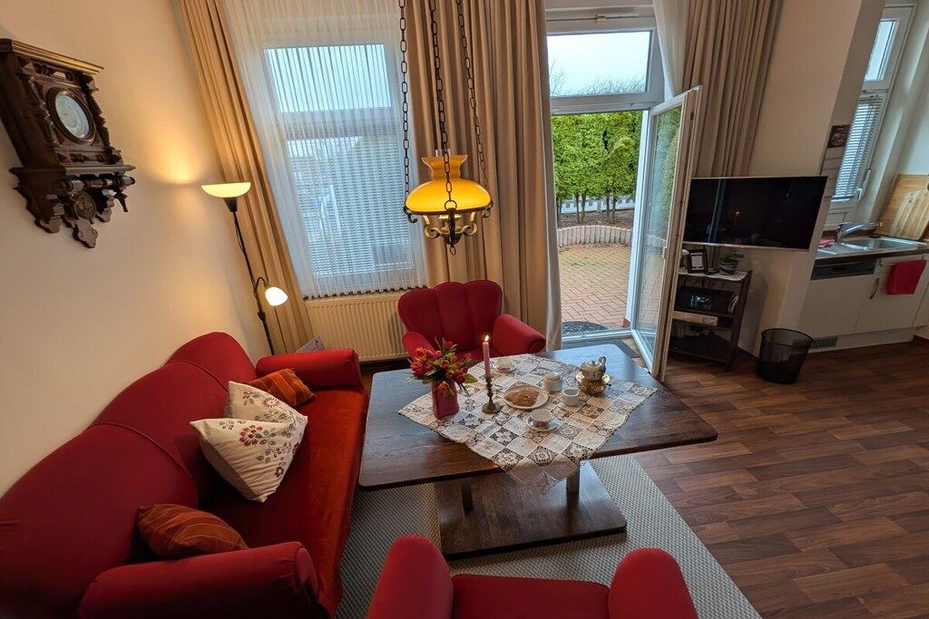 Een woonkamer met een rode bank, een bijzettafeltje met een bloemrijk tafelkleed, en een televisie in de hoek.