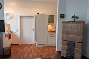 A compact kitchen with a white refrigerator, a microwave, and a sink. There's a clock on the wall and a small plant on top of the refrigerator. - Holiday apartment with 2 bedrooms (Norderney)