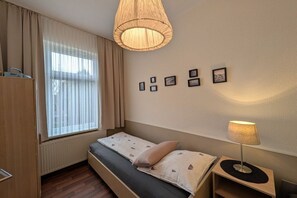Une chambre à coucher avec un lit, une lampe de chevet, une fenêtre avec des rideaux, un radiateur et un mur orné de tableaux.