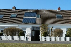 A residential building with a tiled roof, solar panels, a white picket fence, and a black door. - Holiday apartment with 2 bedrooms (Norderney)