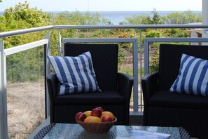 Zwei Korbstühle mit Streifenpolstern, ein Korbkorb mit Obst und ein Tisch auf einem Balkon mit Meerblick.