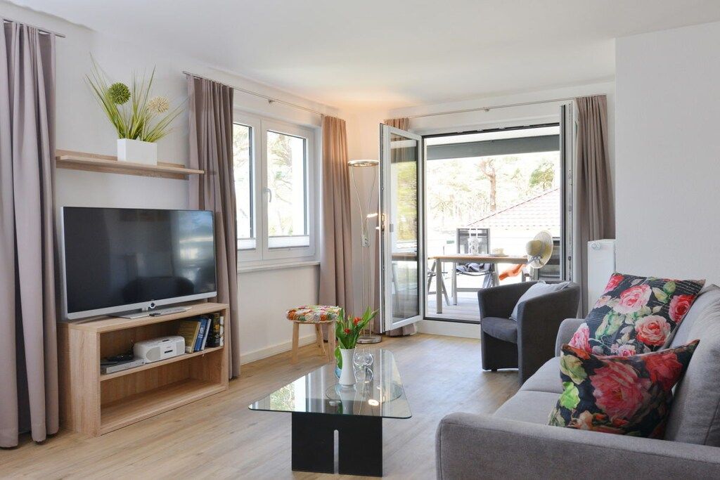 Ein modernes Wohnzimmer mit Fernseher, Glastisch und einer Couch mit floralen Kissen.