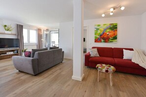 Ein modernes Wohnzimmer mit einem grauen Sofa, einem roten Sofa, einem Fernseher und einem farbenfrohen Vogelbild an der Wand.