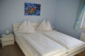 A double bed with white bedding, a bedside table with a lamp, and a painting on the wall. - Holiday apartment with 1 bedroom (Zingst)