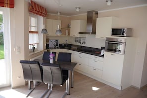 A modern kitchen with white cabinets, a stainless steel oven, and a dining area with a table and chairs. - Holiday apartment with 1 bedroom (Zingst)