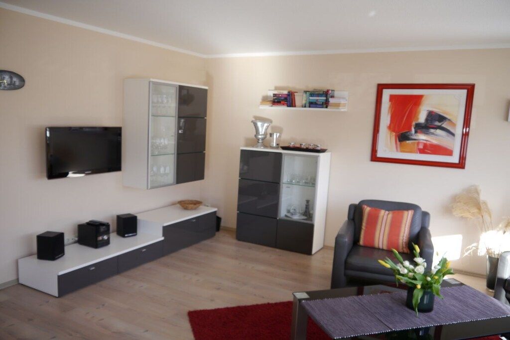 A modern living room with a flat-screen TV, built-in cabinets, a bookshelf, a red rug, and a framed abstract painting.