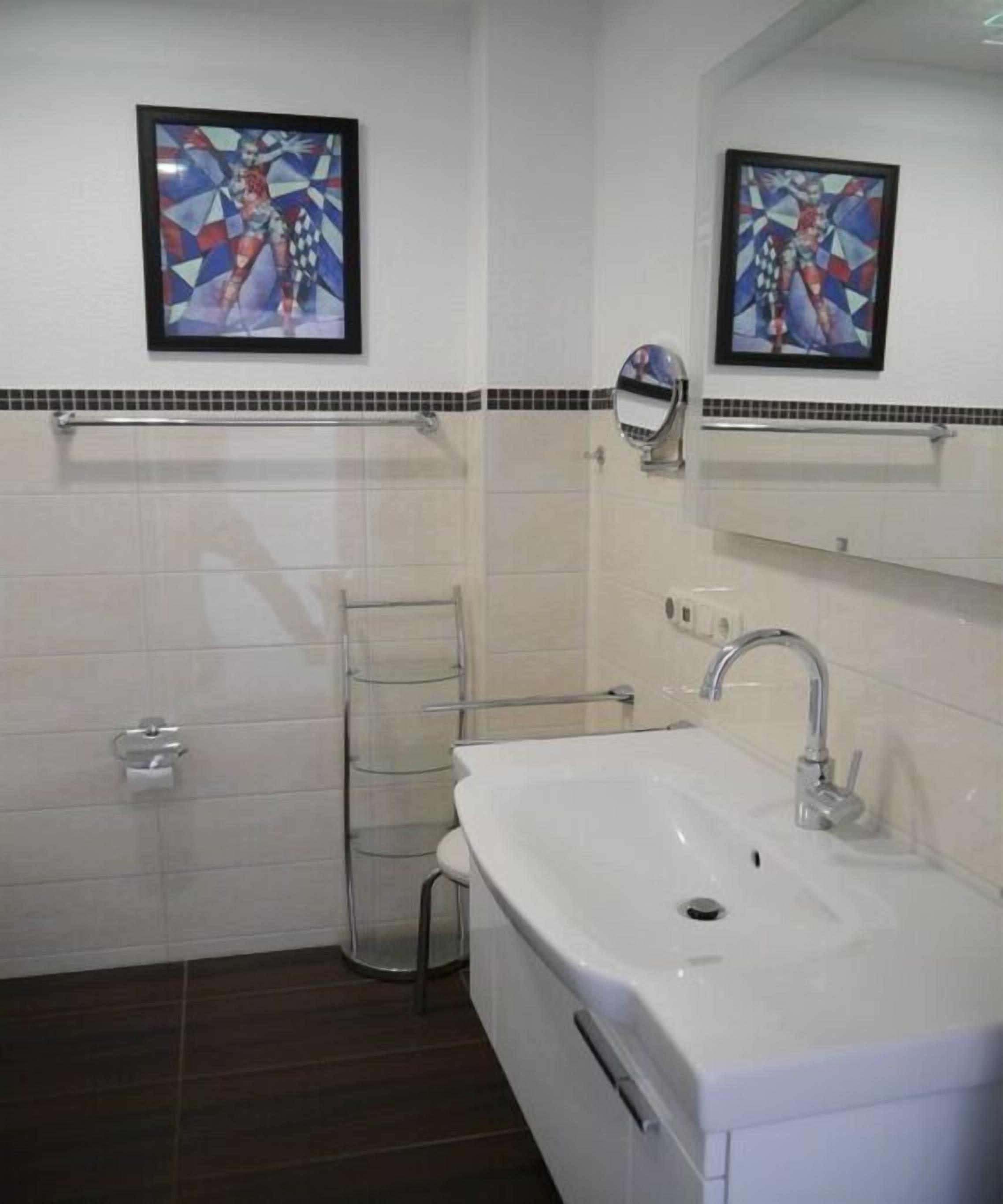 Un baño con un lavamanos blanco, un perchero y dos cuadros en la pared.