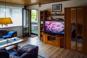 A living room with a television, wooden furniture, and a sliding glass door leading to an outdoor area. - Holiday apartment with 1 bedroom (Bad Zwischenahn)