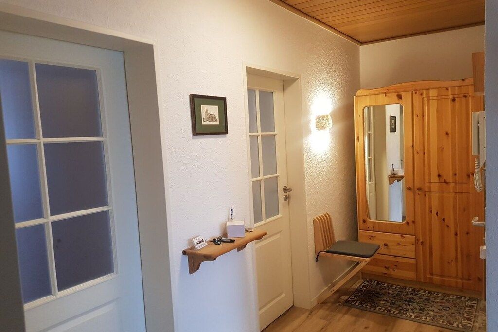 A hallway with a wooden door, a bench, a small shelf with items, and a framed picture on the wall.