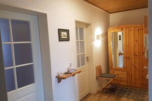 Ein Flur mit einer Holztür, einer Bank, einem kleinen Regal mit Gegenständen und einem gerahmten Bild an der Wand.