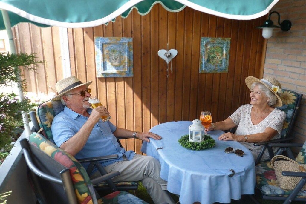 Zwei Personen sitzen an einem Tisch im Freien mit Getränken, umgeben von Holzverkleidungen und Dekorationselementen.