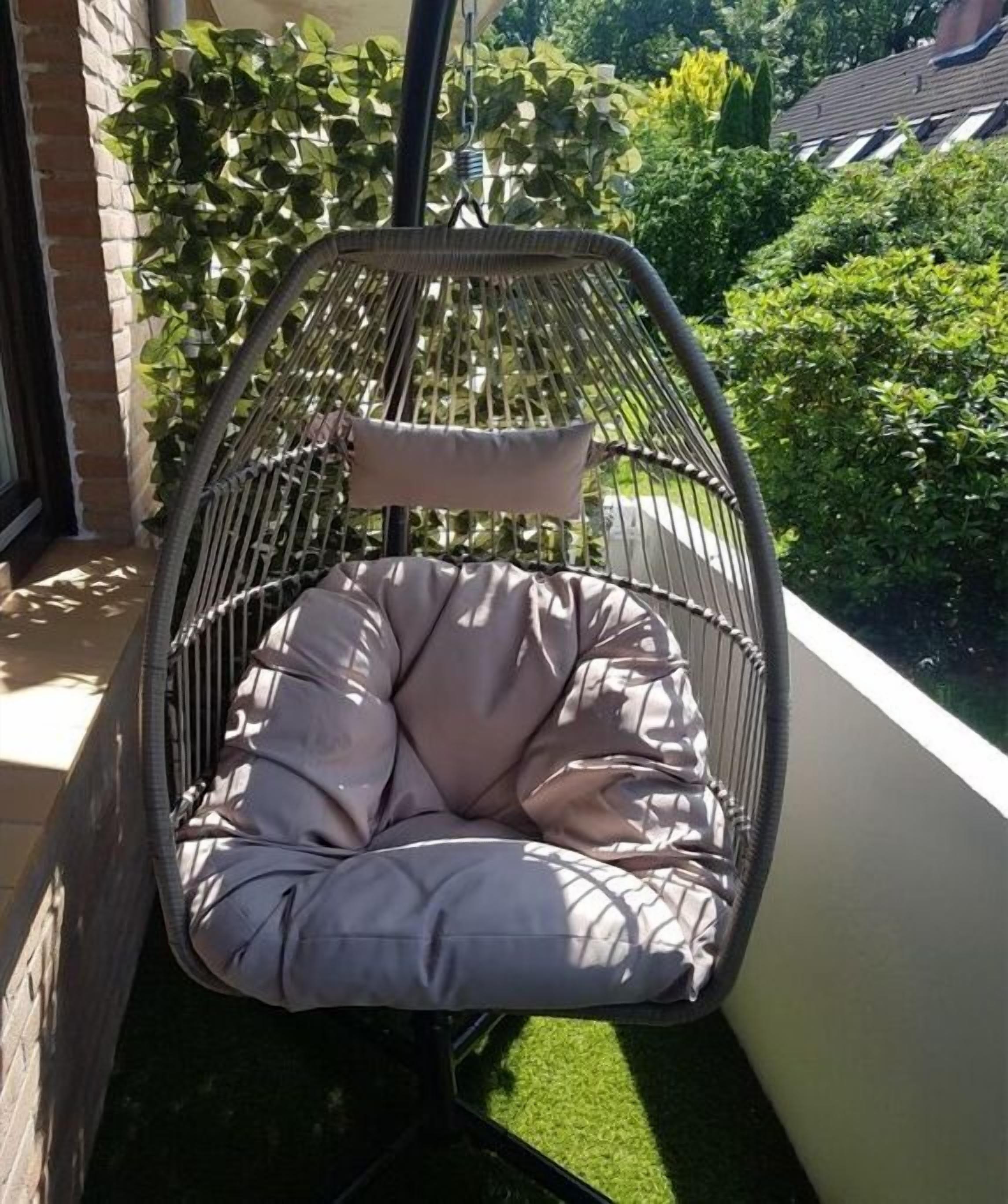 A wicker chair with cushions on a balcony with a view of greenery and a building.