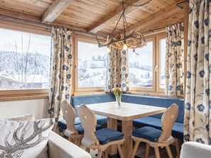 Ein gemütliches Zimmer mit Holzbalkendecke, einem runden Tisch mit blau gepolsterten Stühlen und einer Bank mit blauen Kissen.