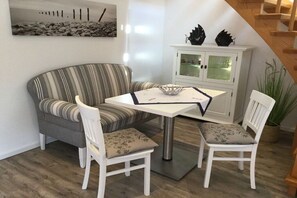 A dining area with a striped sofa, two white chairs, a white table with a decorative bowl, and a cabinet with glass doors. - Holiday apartment with 2 bedrooms (Norddeich)