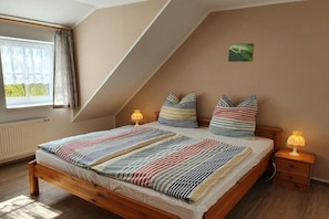 A bedroom with a sloped ceiling, a bed with striped bedding, two bedside lamps, and a window with curtains. - in the Damaris house || Zingst (Zingst)