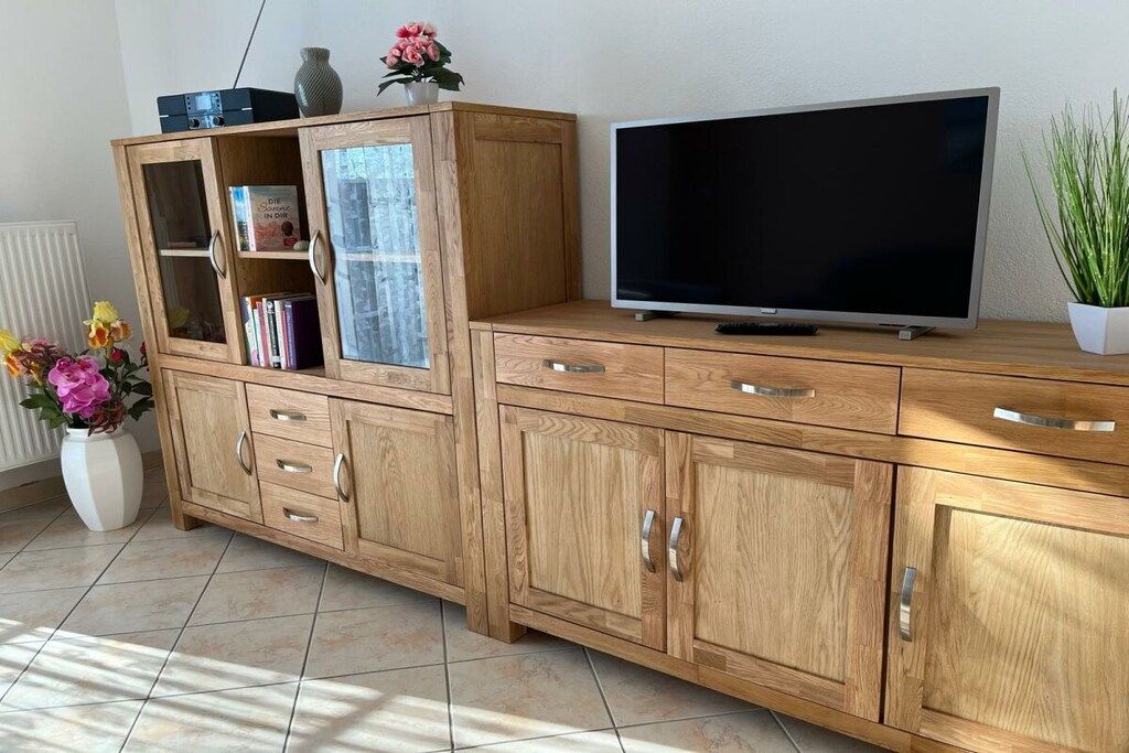 Ein Holzschrank mit mehreren Schubladen und Regalen, ein Flachbildfernseher darauf und eine Topfpflanze daneben.