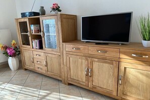 A wooden cabinet with multiple drawers and shelves, a flat-screen TV on top, and a potted plant beside it. - in the Damaris house || Zingst (Zingst)