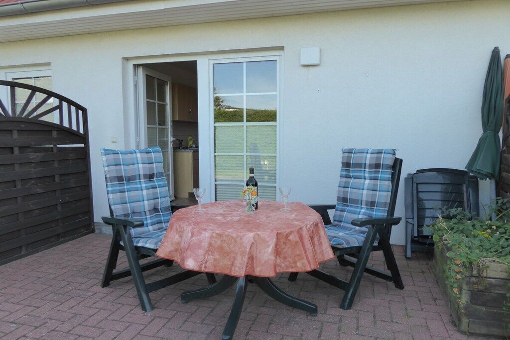 Patio esterno con due sedie, un tavolo, un cancello e l'ingresso di un edificio.