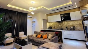A modern living room with a sofa, ottoman, and a dining area with a kitchen in the background. - Pearl Island Haven (Port Harcourt)