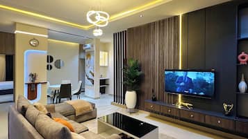A modern living room with a sofa, coffee table, TV, and a dining area in the background.