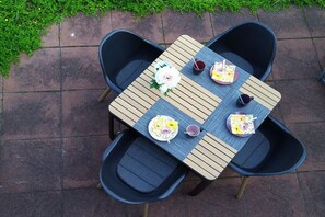 Een vierkante tafel met vier stoelen, elk met een kussen. Op de tafel staat een bloemstuk en twee borden met bestek.