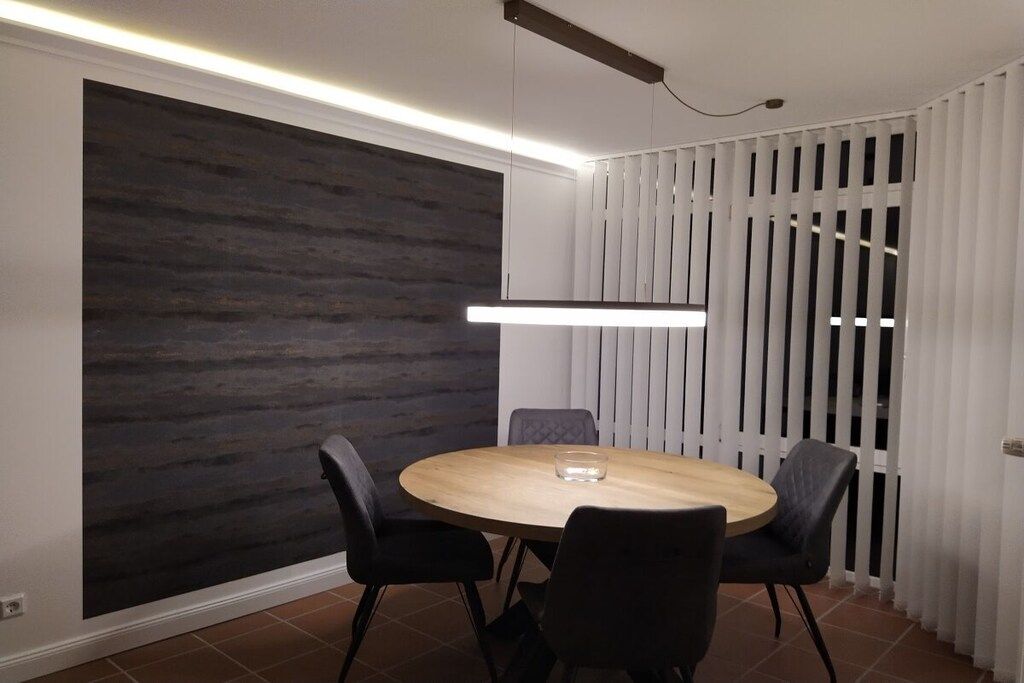 Un espace repas moderne avec une table ronde et quatre chaises, un mur texturé de couleur sombre et une cloison blanche avec des lattes verticales.
