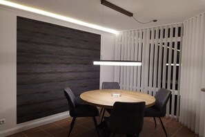Een moderne eetruimte met een ronde tafel en vier stoelen, een donkere, gestructureerde wand en een witte scheidingswand met verticale lamellen.