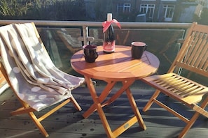 A wooden deck with a round table and two chairs, a bottle of wine, and two mugs. - Holiday home with 1 bedroom (Bad Zwischenahn)