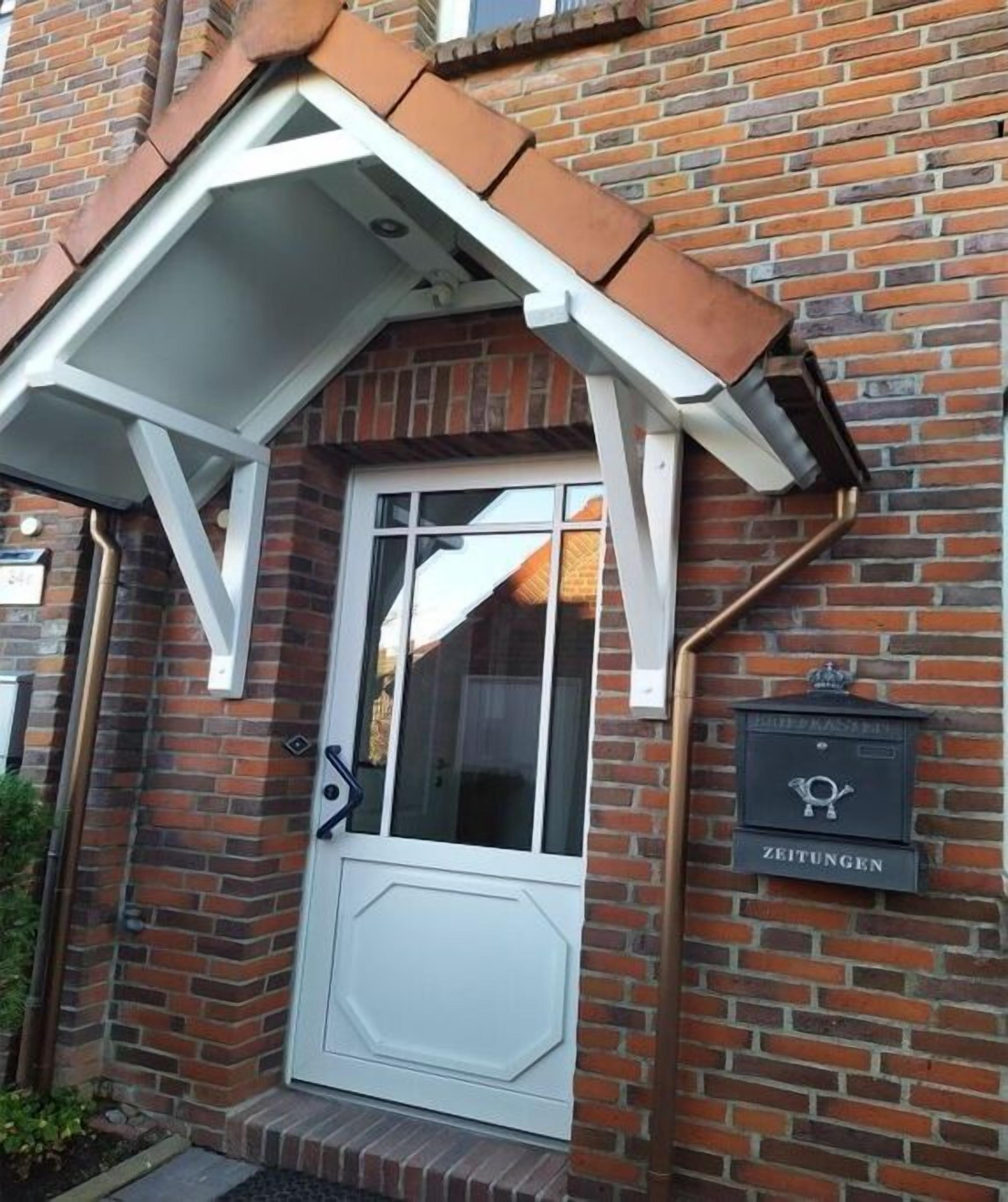 Ein Backsteinhaus mit einer weißen Tür und einer kleinen Markise. An der Wand befindet sich ein Schild mit der Aufschrift 'ZEITUNGEN'.