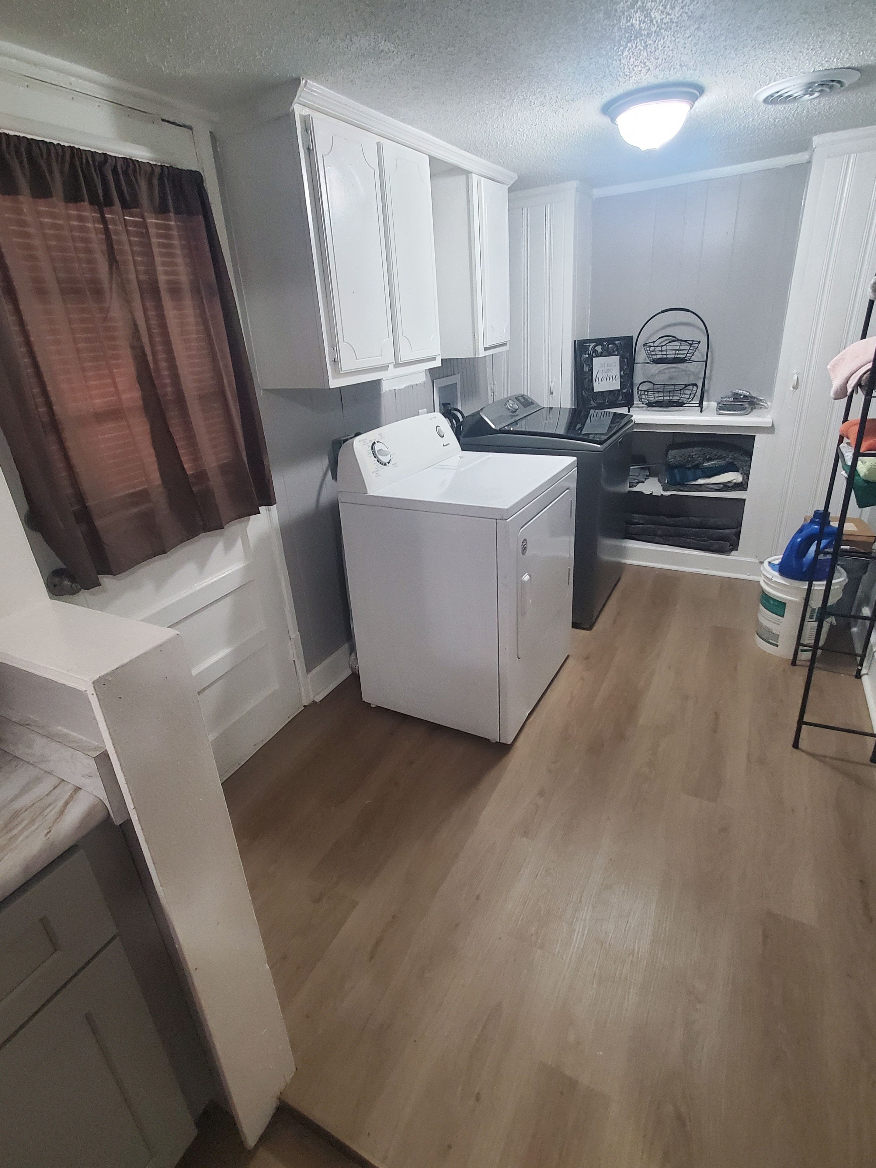 A compact kitchen with white cabinets, a washing machine, a small countertop, and a ceiling light fixture.