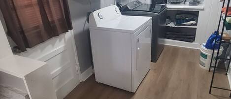 A compact kitchen with white cabinets, a washing machine, a small countertop, and a ceiling light fixture.