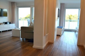 A modern hotel room with a wooden floor, a flat-screen TV, a sofa, and a balcony with a view. - Holiday apartment with 1 bedroom (Dierhagen)