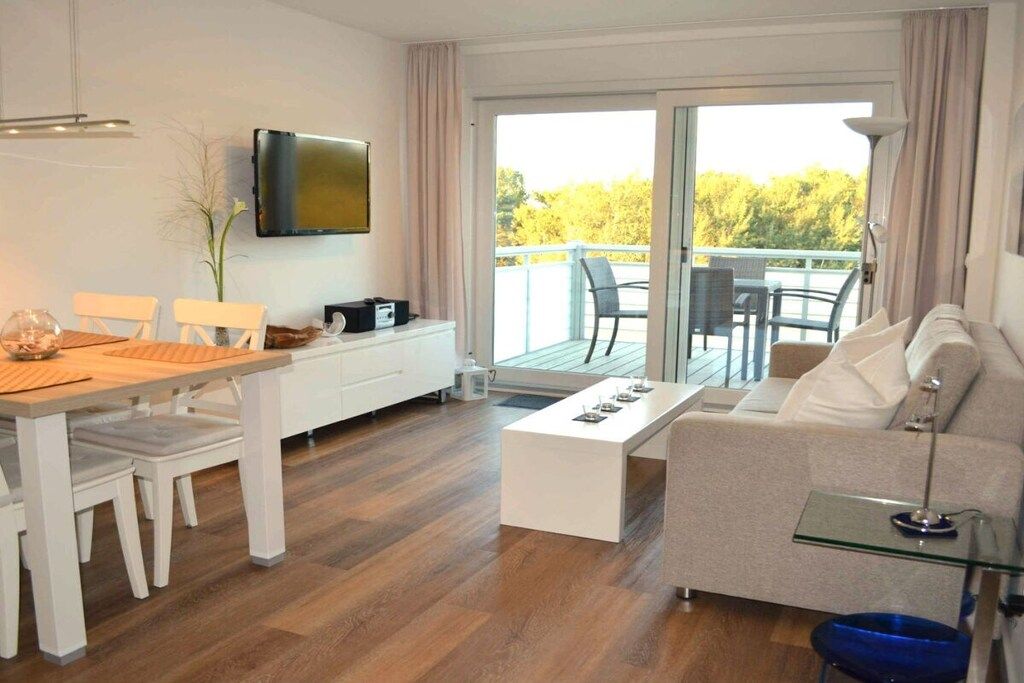 A modern living room with a dining area, a sofa, a coffee table, and a TV mounted on the wall.
