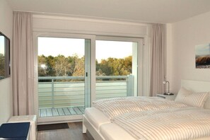 Ein Hotelzimmer mit Bett, Nachttisch, Lampe und Blick ins Freie durch eine Schiebetür.