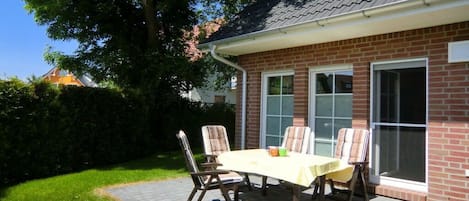A patio with a table and chairs, a brick house, and a large tree.