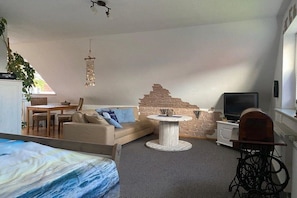 A room with a sofa, a round table, a television, and a brick wall. - Holiday apartment Hehl (Born)