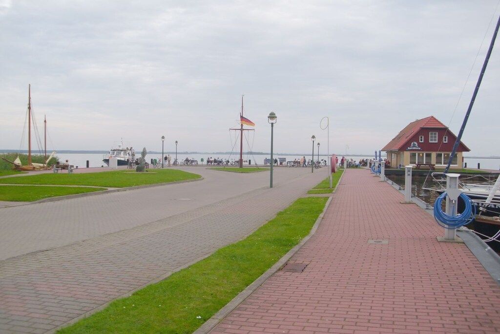 Un paseo marítimo con un edificio de techo rojo, un asta de banderas y un muelle para embarcaciones.