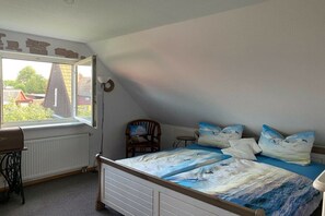A bedroom with a bed, a chair, a sewing machine, and a window with a view of houses. - Holiday apartment Hehl (Born)