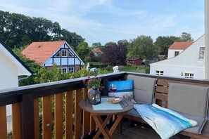 A deck with a wooden railing, a round table with a cushion, a flower vase, and a glass of red wine. - Holiday apartment Hehl (Born)