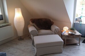 A room with a sloped ceiling, a large floor lamp, a cushioned chair, a small ottoman, and a wooden side table with a lamp. - Holiday home in Maasholm with swimming pool (Maasholm)