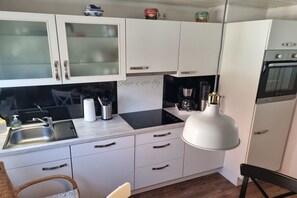 A compact kitchen with white cabinets, a black countertop, a built-in oven, and a hanging pendant light. - Holiday home in Maasholm with swimming pool (Maasholm)