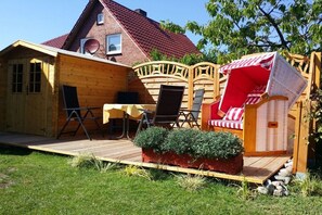A wooden deck with a table and chairs, a small seating area with a red and white striped cushion, and a potted plant. - Holiday home in Maasholm with swimming pool (Maasholm)