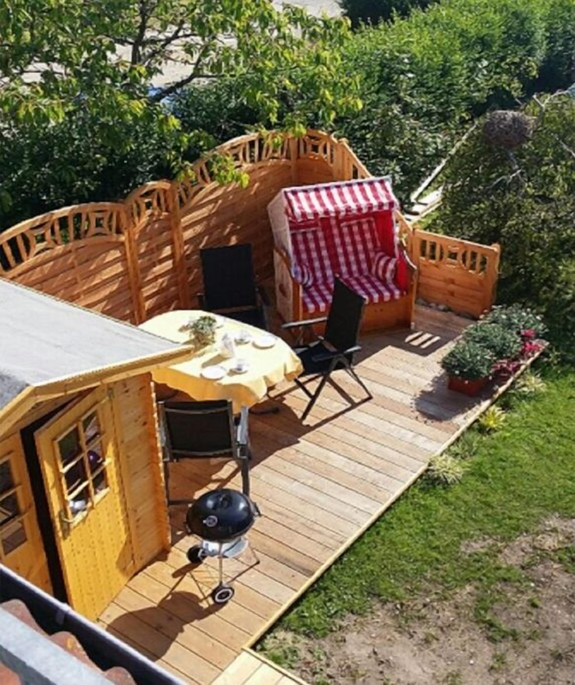 Un terrazzo in legno con tavolo e sedie, un barbecue e un piccolo deposito.