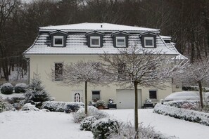 A two-story house with a snow-covered roof, a garage, and a garden with snow-covered bushes and trees. - Holiday apartment with 1 bedroom (Quedlinburg \/ OT Bad Suderode)