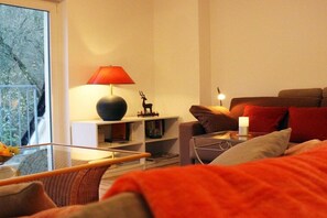 Una sala de estar con una mesa de centro de vidrio, un sofá, una lámpara roja y una estantería.
